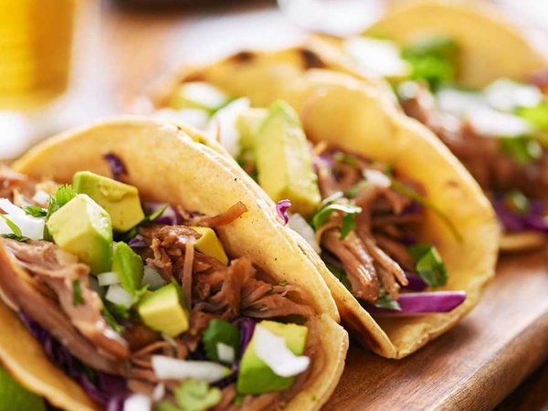 three pork carnitas street tacos in yellow corn tortilla with avocado, onion, cilantro and cabbage