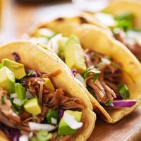 three  pork carnitas street tacos in yellow corn tortilla with avocado, onion, cilantro and cabbage