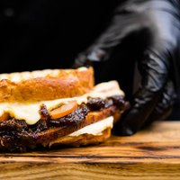 Professional catering. Chef hands serving smoked turkey breast sandwich on wooden board.