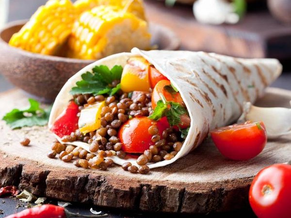 Vegan tortilla wrap, roll with grilled vegetabes and lentil and boiled corn cob on a wooden background