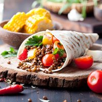 Vegan tortilla wrap, roll with grilled vegetabes and lentil and boiled corn cob on a wooden background