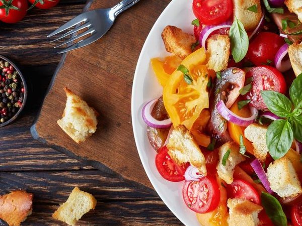 delicious fresh classic italian salad panzanella with tomatoes, croutons basil and onion rings on a white plate on an old wooden table with ingredients, view from above, flat lay, close-up