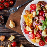 delicious fresh classic italian salad panzanella with tomatoes, croutons basil and onion rings on a white plate on an old wooden table with ingredients, view from above, flat lay, close-up