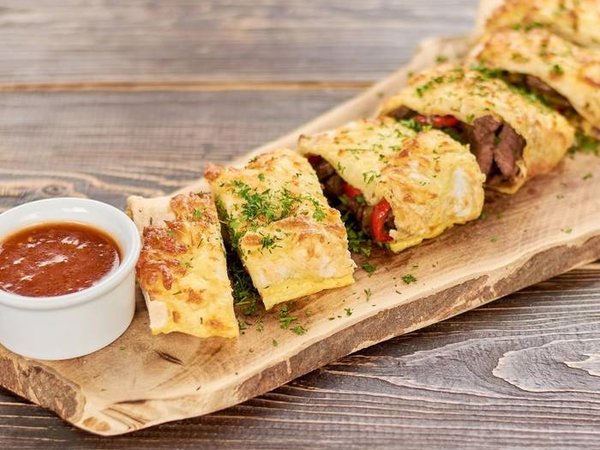 Spicy mexican burrito with sauce. Delicious burrito brunch cutted in pieces and served with fresh chili pepper with basil.