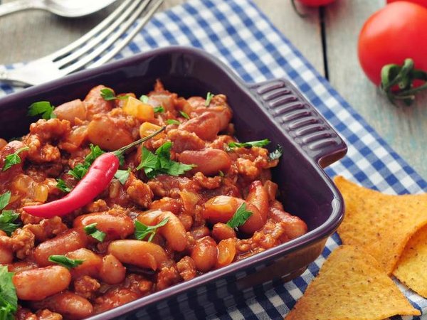 Chili Con Carne in baking mold with tortilla chips on wooden table