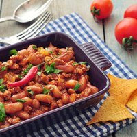 Chili Con Carne in baking mold with tortilla chips on wooden table