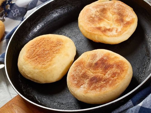 cooking breakfast - baking english muffins on a skillet and are chilling on a grid on wooden table with kitchen towel, fresh butter and knife, view from above, close-up
