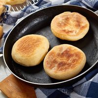cooking breakfast - baking english muffins on a skillet and are chilling on a grid on wooden table with kitchen towel, fresh butter and knife, view from above, close-up