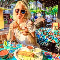 Joyful blonde woman puts enchilada in chili sauce, at typical Mexican food, at traditional restaurant of El Pueblo, Olvera street, Los Angeles Downtown State Historic Park, California, United States.