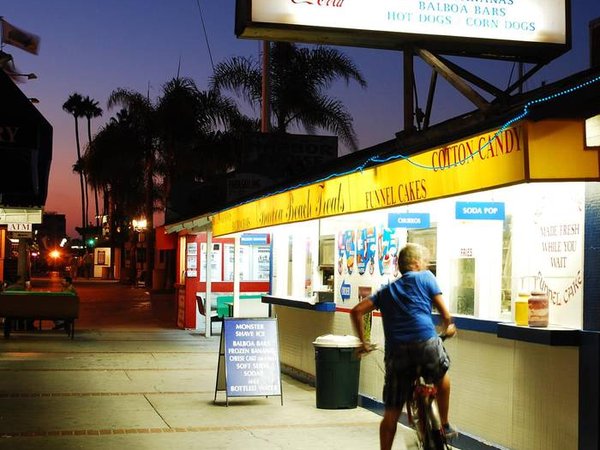 A teenage boy bikes up to an ice cream stand in Newport Beach California at dusk