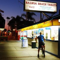 A teenage boy bikes up to an ice cream stand in Newport Beach California at dusk