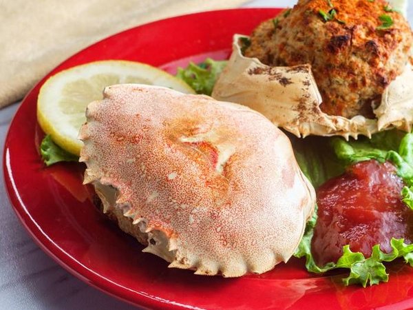 Stuffed seasoned crab shells garnished with romaine lettuce and sliced lemon with cocktail sauce
