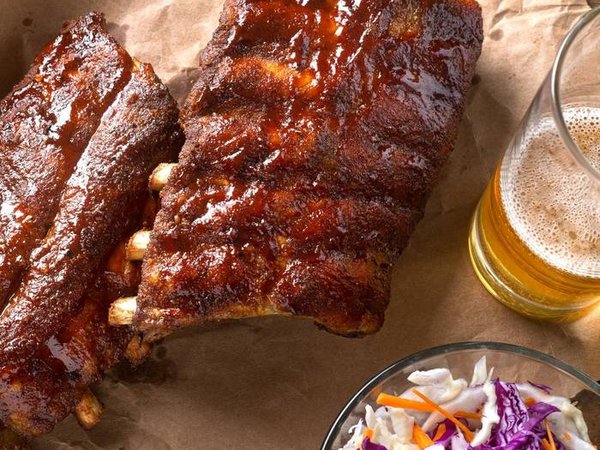 A rack of delicious baby back ribs with barbecue sauce, french fries, coleslaw and beer.
