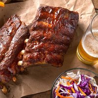 A rack of delicious baby back ribs with barbecue sauce, french fries, coleslaw and beer.