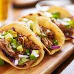 three  pork carnitas street tacos in yellow corn tortilla with avocado, onion, cilantro and cabbage