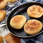 cooking breakfast - baking english muffins on a skillet and are chilling on a grid on wooden table with kitchen towel, fresh butter and knife, view from above, close-up